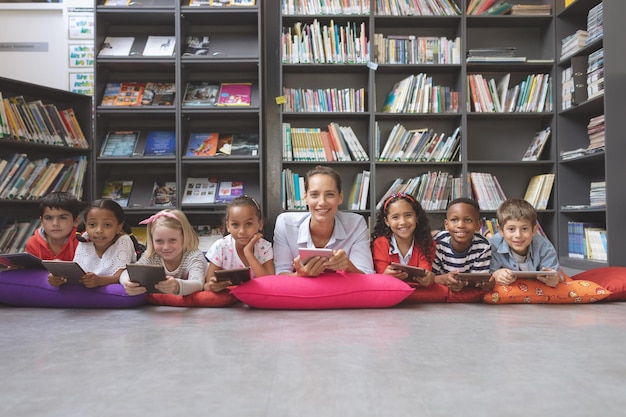 Gelukkige onderwijzeres die met zijn schoolkinderen in een bibliotheek ligt