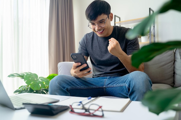 Foto gelukkige opgewonden man die naar zijn mobiele telefoon kijkt man die goed nieuws ontvangt met behulp van een smartphone thuis