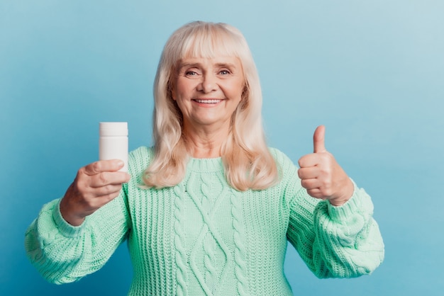 Gelukkige oude dame houdt pillenpot vast en toont fijn gebaar geïsoleerd op blauwe achtergrond