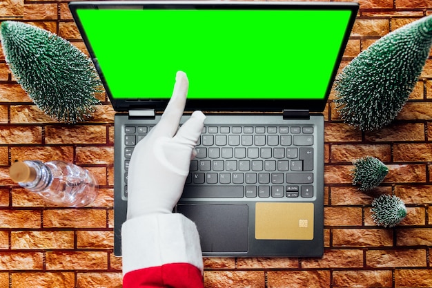 Gelukkige oude kerstman met hoed die een geschenkdoos vasthoudt met behulp van een laptopcomputer die laat op een vrolijke kerstavond aan de thuistafel van de workshop zit. e-commerce website kerstmis vakantie online winkelen e-commerce verkoop