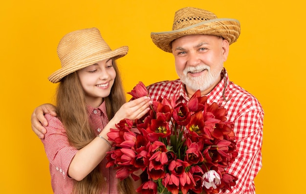 Gelukkige oude opa met kleinkind houdt tulp bloemen op gele achtergrond