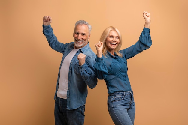 Gelukkige oudere man en vrouw die succes vieren op beige