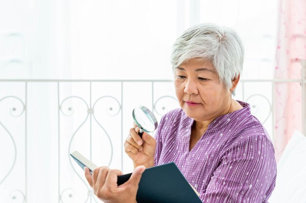 Gelukkige oudere senior vrouw vrouwelijke dame geniet van het lezen van een boek met vergrootglas