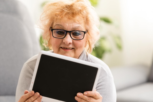 Gelukkige oudere vrouw die een tablet gebruikt en lacht