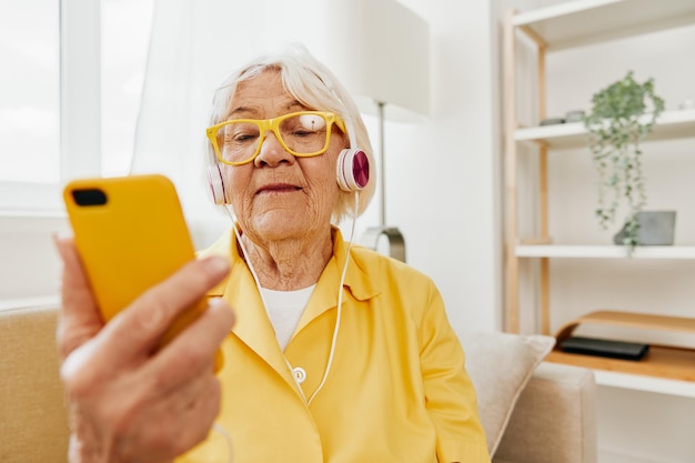 Gelukkige oudere vrouw die een videogesprek op haar telefoon bekijkt en naar muziek luistert op haar hoofdtelefoon heldere moderne interieur levensstijl online communicatie