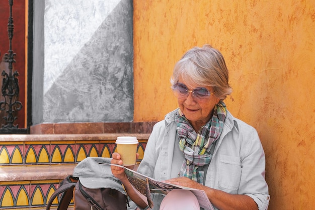 Gelukkige oudere vrouw die op een trap zit en een kaart raadpleegt met een afhaalkoffie oudere reizigersdame die geniet van vrije tijd of pensioen