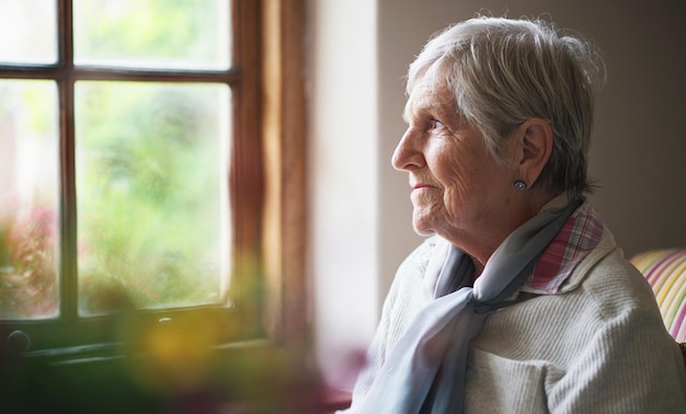 Gelukkige oudere vrouw die uit het raam kijkt en denkt aan herinneringen gepensioneerde levensstijl concept