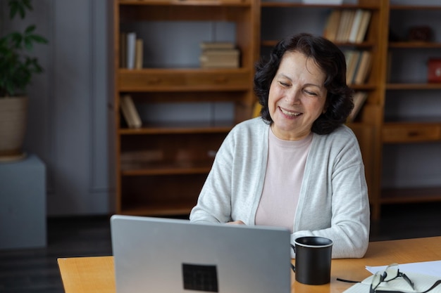 Gelukkige oudere vrouw van middelbare leeftijd zit met laptop te praten tijdens een videogesprek met familie van vrienden Lachende volwassen oude senior grootmoeder die plezier heeft tijdens het praten met volwassen kinderen online