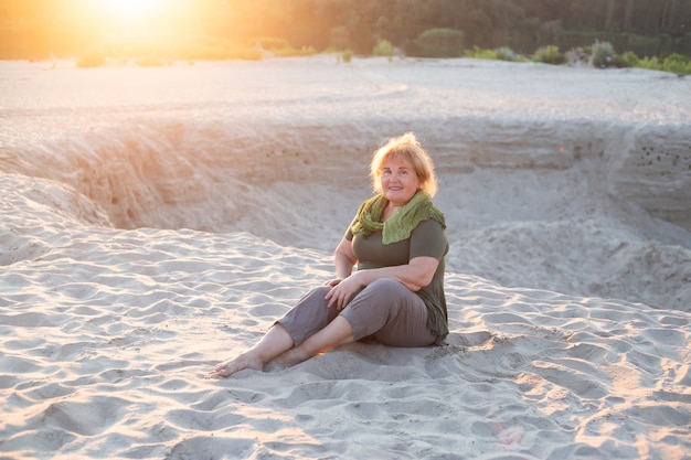 Gelukkige oudere vrouwenzitting op een zand buiten in de zomer