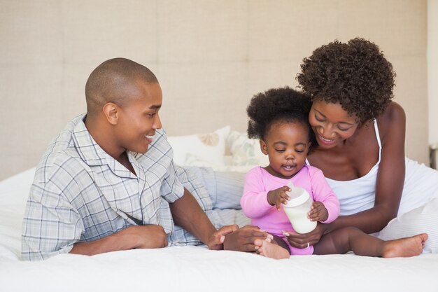 Gelukkige ouders en babymeisjeszitting op bed samen