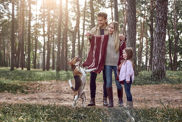 Gelukkige ouders hebben plezier met hun dochter en springende hond in het bos