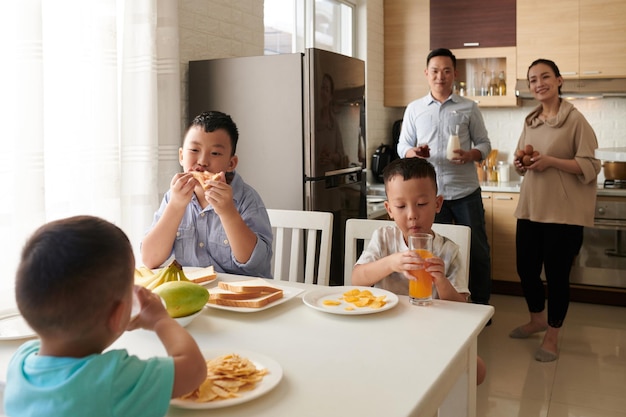 Gelukkige ouders kijken naar hun drie zonen die ontbijten aan de keukentafel