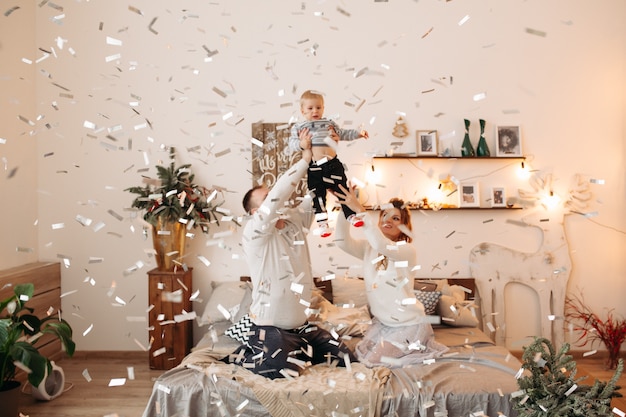 Gelukkige ouders met schattig kindje staan samen in prachtige studio, knuffelen, voorzijde kijken en poseren