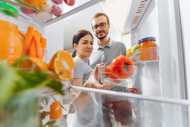 Gelukkige paar in de buurt van open koelkast met groenten en fruit. gezonde voeding concept.