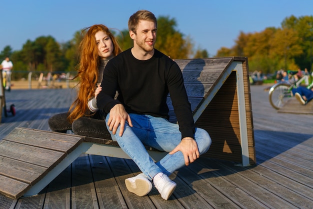 gelukkige paar jongen en meisje met lang rood haar zitten op een houten dek in een omhelzing jonge ma