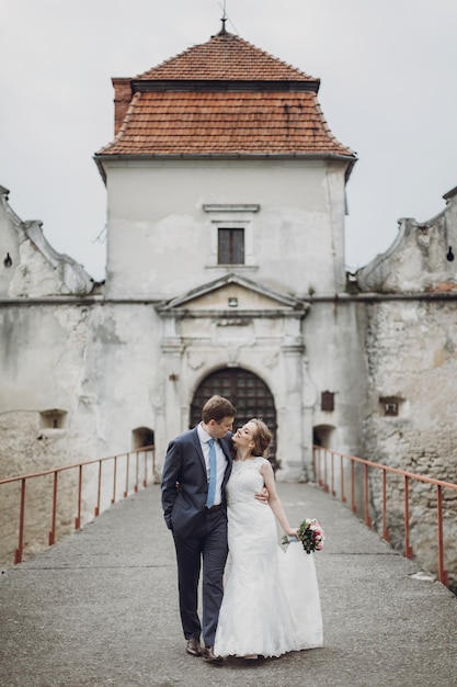Gelukkige paar jonggehuwden wandelen in de buurt van kasteel sprookjesachtig huwelijksmoment mooie bruid en bruidegom knuffelen in de buurt van de ingang van het oude kasteel in Europa