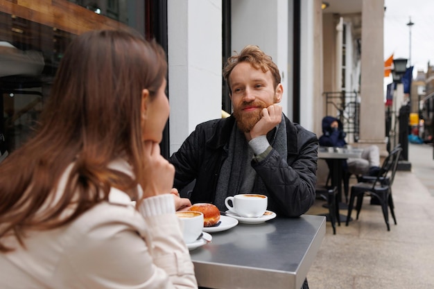 Gelukkige paar koffie drinken en lachen met elkaar praten zittend aan de tafel van outdoor cafe op straten van de stad