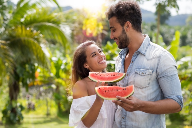 Gelukkige paar omhelzen elkaar kijken Hold watermeloen Slice buiten in tropische attractiepark