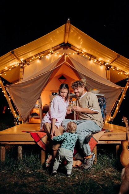 Gelukkige paar ontspannen in glamping op zomeravond en wijn drinken in de buurt van gezellig vreugdevuur Luxe kampeertent voor openluchtrecreatie en recreatie Lifestyle concept