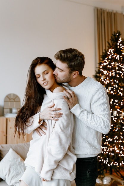 gelukkige paar verliefd in een witte, gezellige woonkamer met kerstversiering en een kerstboom