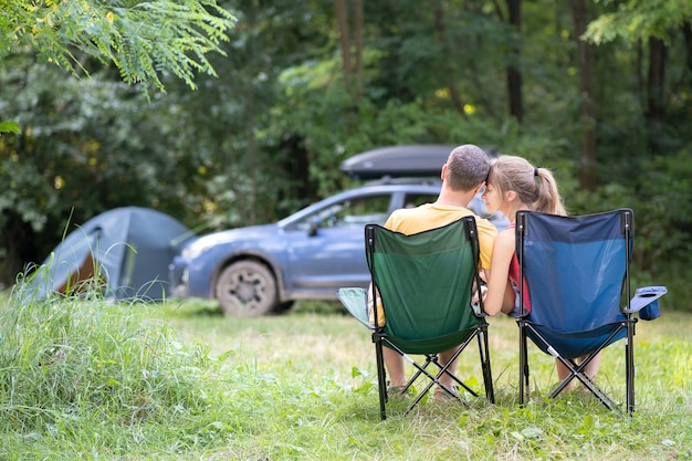 Gelukkige paar zittend op stoelen op camping knuffelen elkaar. Reizen, kamperen en vakanties concept.