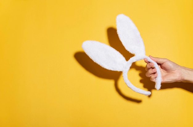 Gelukkige pasen-hand die witte konijntjesoren op gele decoratie houden als achtergrond in de ruimte van het vakantieexemplaar