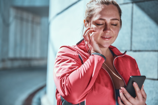 Gelukkige plus size vrouw in koptelefoon met smartphone en muziek luisteren met gesloten ogen