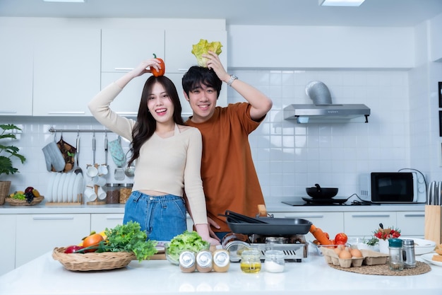 Foto gelukkige portret van liefhebbende jonge aziatische van plezier staan een vrolijke bereiden van eten en genieten koken koken met groenten vlees brood terwijl staan op een keuken condo leven of thuis