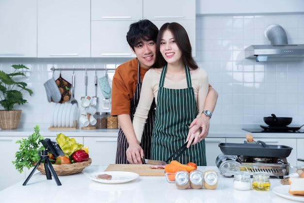 Gelukkige portret van liefhebbende jonge aziatische van plezier staan een vrolijke bereiden van eten en genieten koken koken met groenten vlees brood terwijl staan op een keuken condo leven of thuis