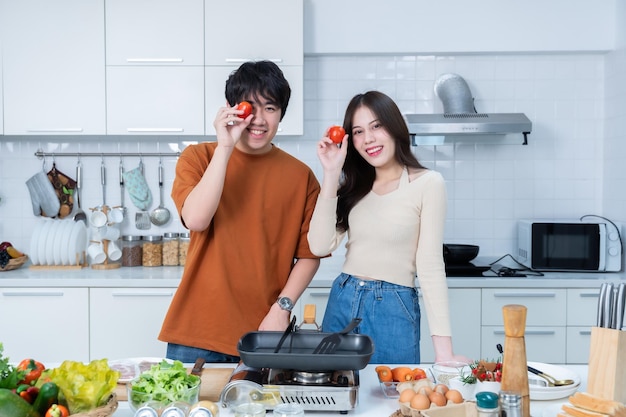 Foto gelukkige portret van liefhebbende jonge aziatische van plezier staan een vrolijke bereiden van eten en genieten koken koken met groenten vlees brood terwijl staan op een keuken condo leven of thuis