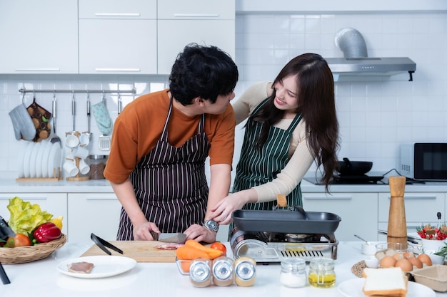 Foto gelukkige portret van liefhebbende jonge aziatische van plezier staan een vrolijke bereiden van eten en genieten koken koken met groenten vlees brood terwijl staan op een keuken condo leven of thuis