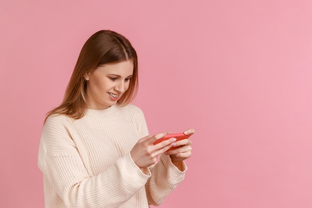 Gelukkige positieve blonde vrouw die een smartphone vasthoudt die videospelletjes speelt en met succes het niveau voltooit