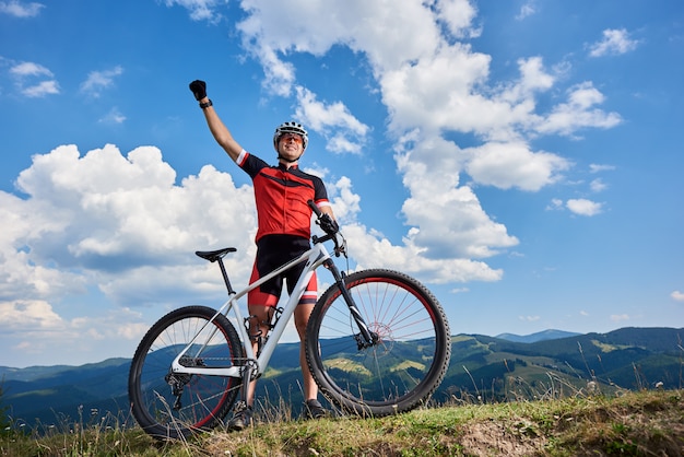 Gelukkige professionele sportmanfietser die zich met fiets in het hele land op een heuvel bevinden