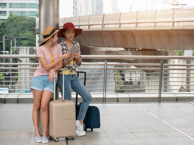 Gelukkige reis samen van twee modieuze meisjes die tablet het serching kaart, vakantie met zakken gebruiken vakantie, reisconcept.