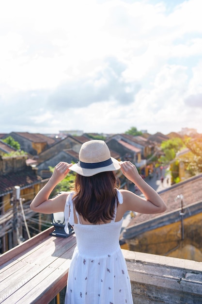 Gelukkige reiziger die reist in Hoi An oude stad in Vietnam vrouw met jurk en hoed sightseeing uitzicht op rooftoplandmark en populair voor toeristische attracties Vietnam en Zuidoost-Azië reisconcept