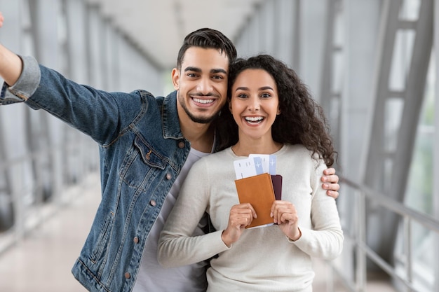 Gelukkige reizigers die een jong Arabisch stel selfie maken op de luchthaven met paspoorten