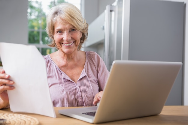 Gelukkige rijpe vrouw die haar laptop met behulp van