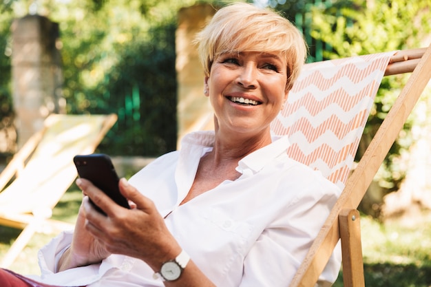 Gelukkige rijpe vrouw die mobiele telefoon met behulp van