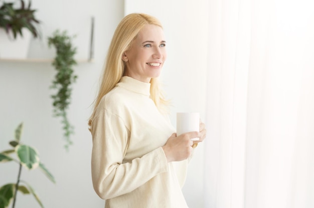 Gelukkige rijpe vrouw die thuis van koffie in de ochtend geniet