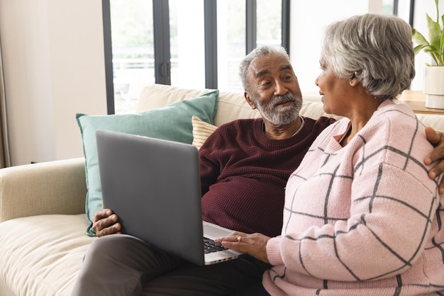 Gelukkige senior biracial paar zitten op de bank en het gebruik van de laptop thuis