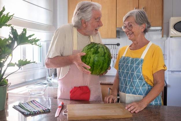 Gelukkige senior blanke echtpaar in de keuken met een grote en zware seizoensgebonden watermeloen