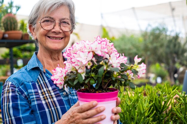 Gelukkige senior blanke vrouw in geruit hemd die geniet van winkelen in de kas en potten met planten en bloemen selecteert voor haar tuin