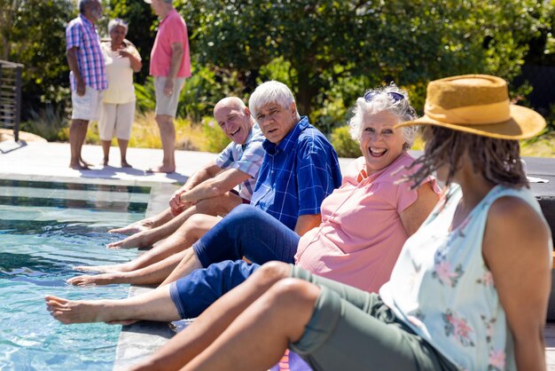 Gelukkige senior diverse mensen zitten bij het zwembad en lachend in de tuin. Senior levensstijl, vriendschap en ontspanning, zomer, pensioen, ongewijzigd.