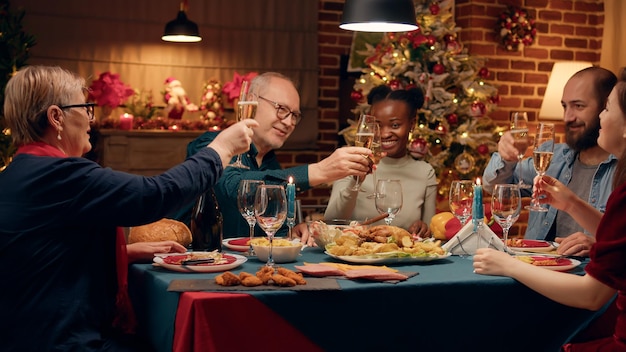 Gelukkige senior man die familieleden uitnodigt om te proosten terwijl hij thuis de wintervakantie viert. feestelijke familieleden kwamen samen om kerstmis te vieren met traditioneel huisgemaakt eten en mousserende wijn.