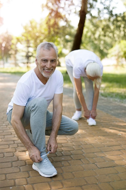 Gelukkige senior man die gaat zitten terwijl hij zijn schoenveters knoopt met zijn vrouw