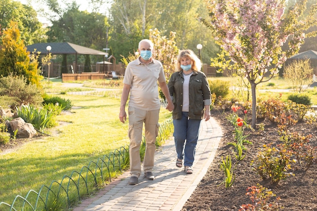 Gelukkige senior paar verliefd dragen van medische masker te beschermen tegen coronavirus. Buiten parkeren.