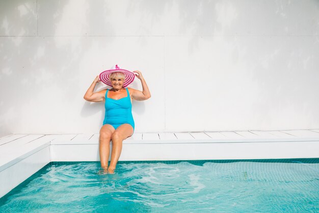 Gelukkige senior vrouw die feest heeft in het zwembad - Mooie senior dame die in de zomer zonnebaadt en ontspant in een privézwembad