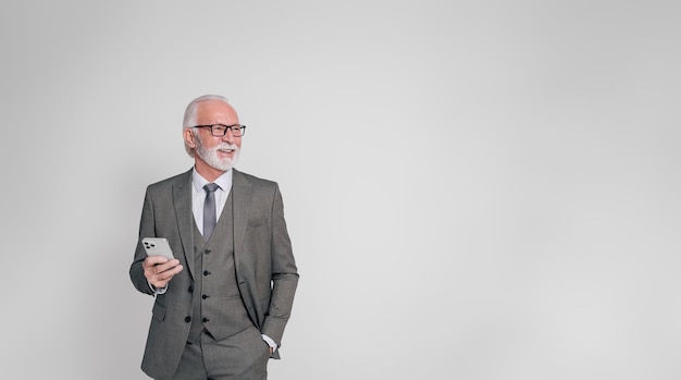 Gelukkige senior zakenman met hand in zak en mobiele telefoon die wegkijkt op een witte achtergrond