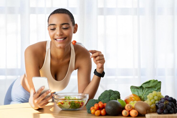 Foto gelukkige slanke jonge latijnse dame in sportkleding eet salade en praat aan de telefoon.
