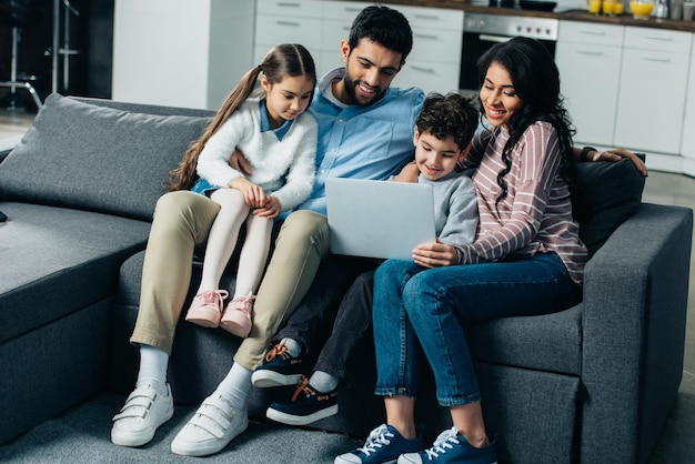gelukkige Spaanse familie zittend op de bank en kijken naar laptop thuis